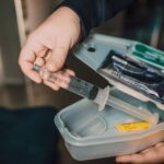 Close-up of a hand holding a syringe from a medical kit with various supplies.
